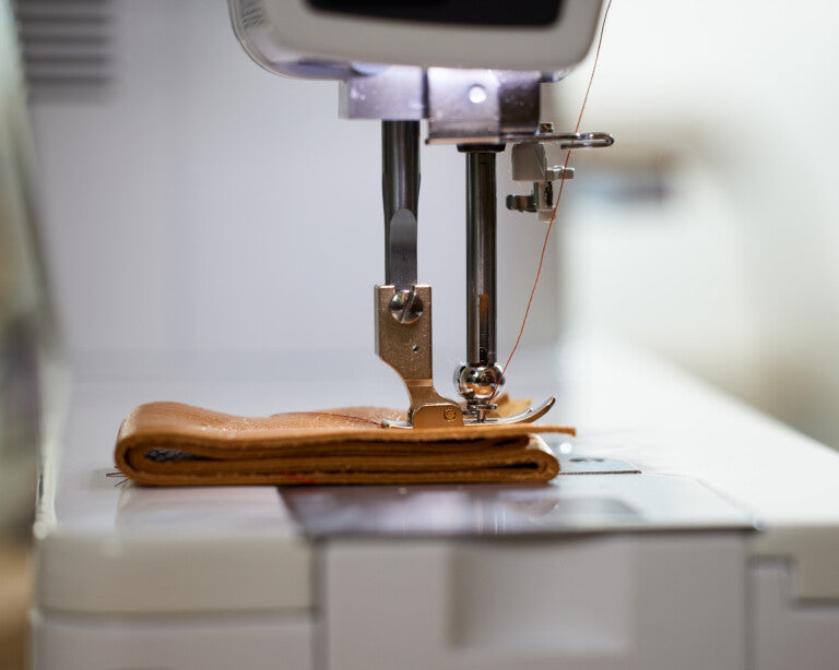 Close up image of a sewing machine stitching together a stack of brown leather material.