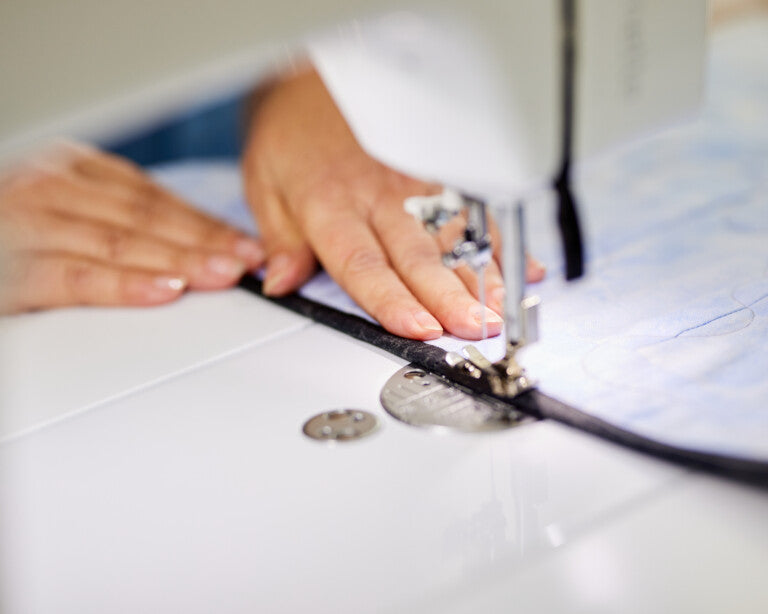 Close up image of hands running a thin, black material through a sewing machine.