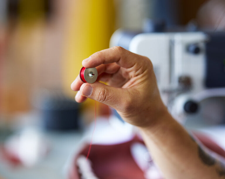 Close up image of a hand holding a small bobbin filled with red thread.