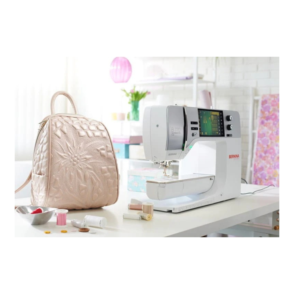 Sewing machine on a table with a beige quilted bag and various items in a bright room.